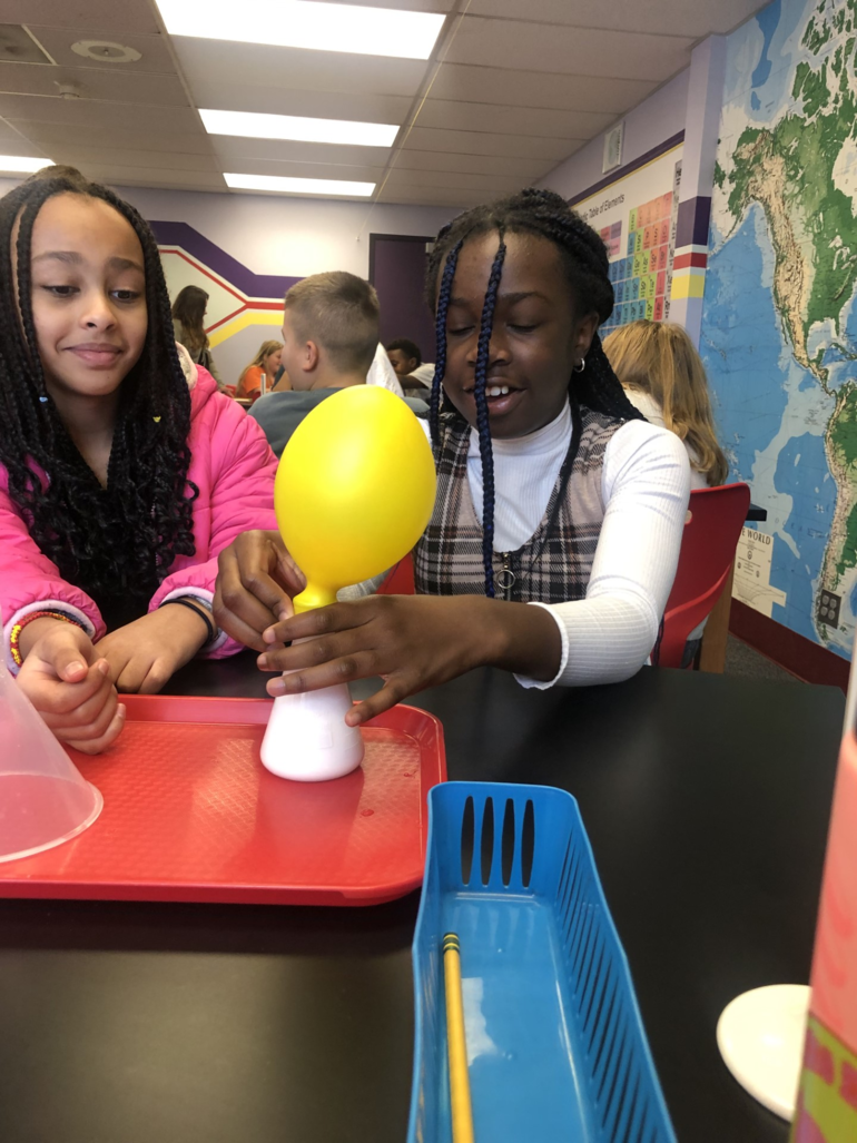 Two girls do an experiment with a balloon.
